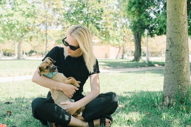 blond haired woman sitting outside in the grass and holding small dog